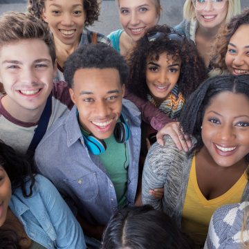 A large group of cheerful diverse young adults looking up and smiling at the camera. The group includes male and female African American, Hispanic and Caucasian ethnicities.